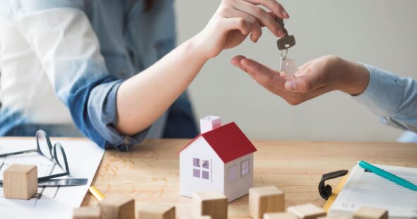 close-up-woman-s-hand-giving-house-key-man-wooden-table